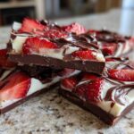 Close-up of stacked pieces of Chocolate Covered Strawberry Bark featuring dark chocolate, white chocolate swirl, and fresh strawberry slices.