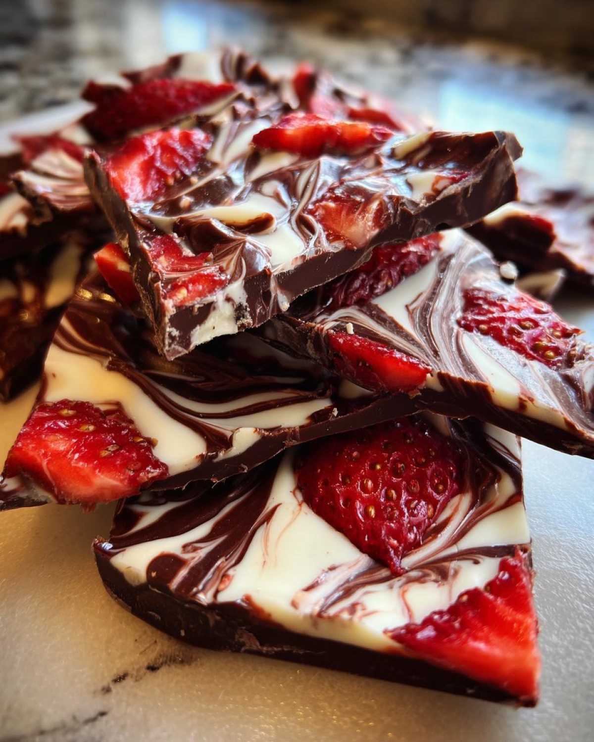 Close-up of stacked pieces of Chocolate Covered Strawberry Bark with dark chocolate, white chocolate swirls, and fresh strawberries.