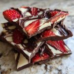 A stack of broken pieces of Chocolate Covered Strawberry Bark featuring dark chocolate, white chocolate swirls, and bright red strawberry slices.