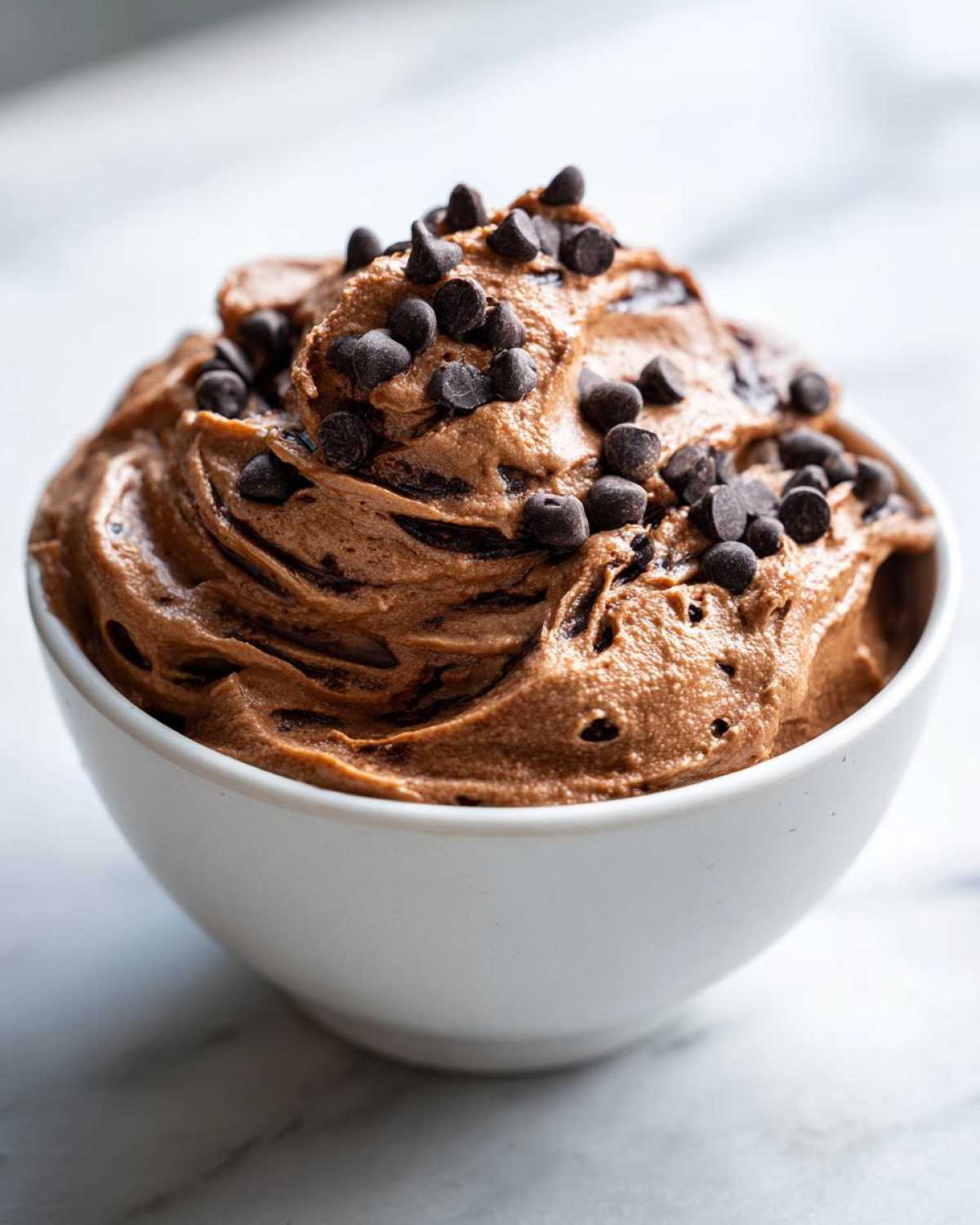 A close-up of thick, swirled Chocolate Peanut Butter Cheesecake Dip topped generously with mini chocolate chips in a white bowl.