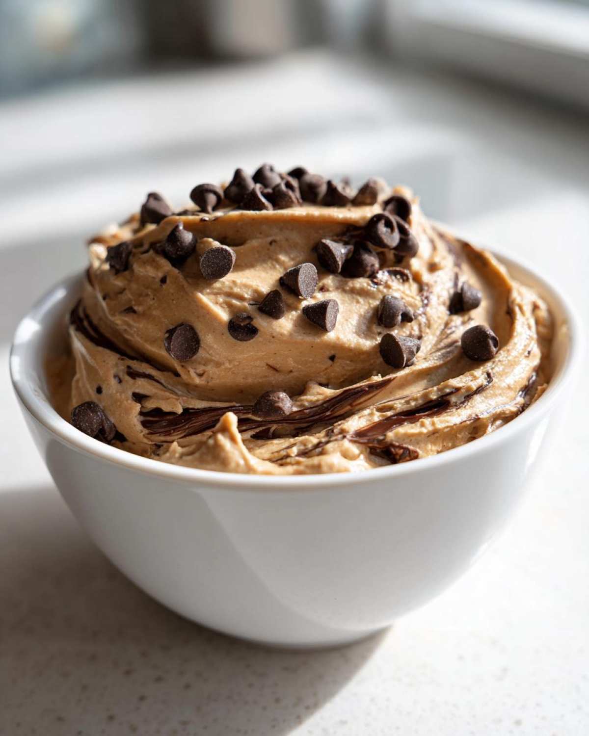 A white bowl filled with creamy Chocolate Peanut Butter Cheesecake Dip, topped with mini chocolate chips.