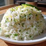 A mound of fluffy white Cilantro Lime Rice garnished with fresh cilantro and lime zest, topped with a lime wedge.