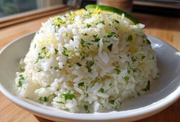 A mound of fluffy white Cilantro Lime Rice garnished with fresh cilantro and lime zest, topped with a lime wedge.