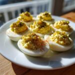 Six halves of Classic Deviled Eggs with Dill Pickle Relish filling, sprinkled with paprika, served on a white plate.