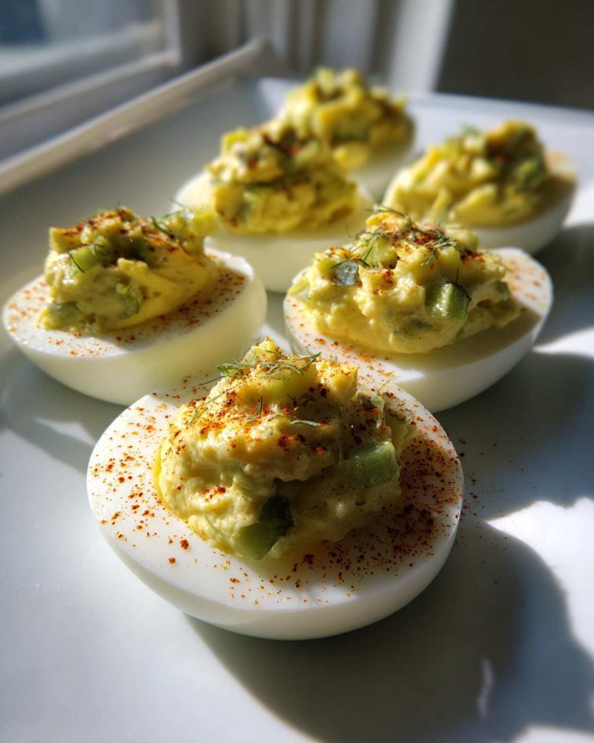Close-up of Classic Deviled Eggs with Dill Pickle Relish, garnished with paprika and dill, sitting on a white plate.