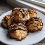 Five golden-brown Coconut Macaroons with Dark Chocolate Drizzle arranged on a white plate.