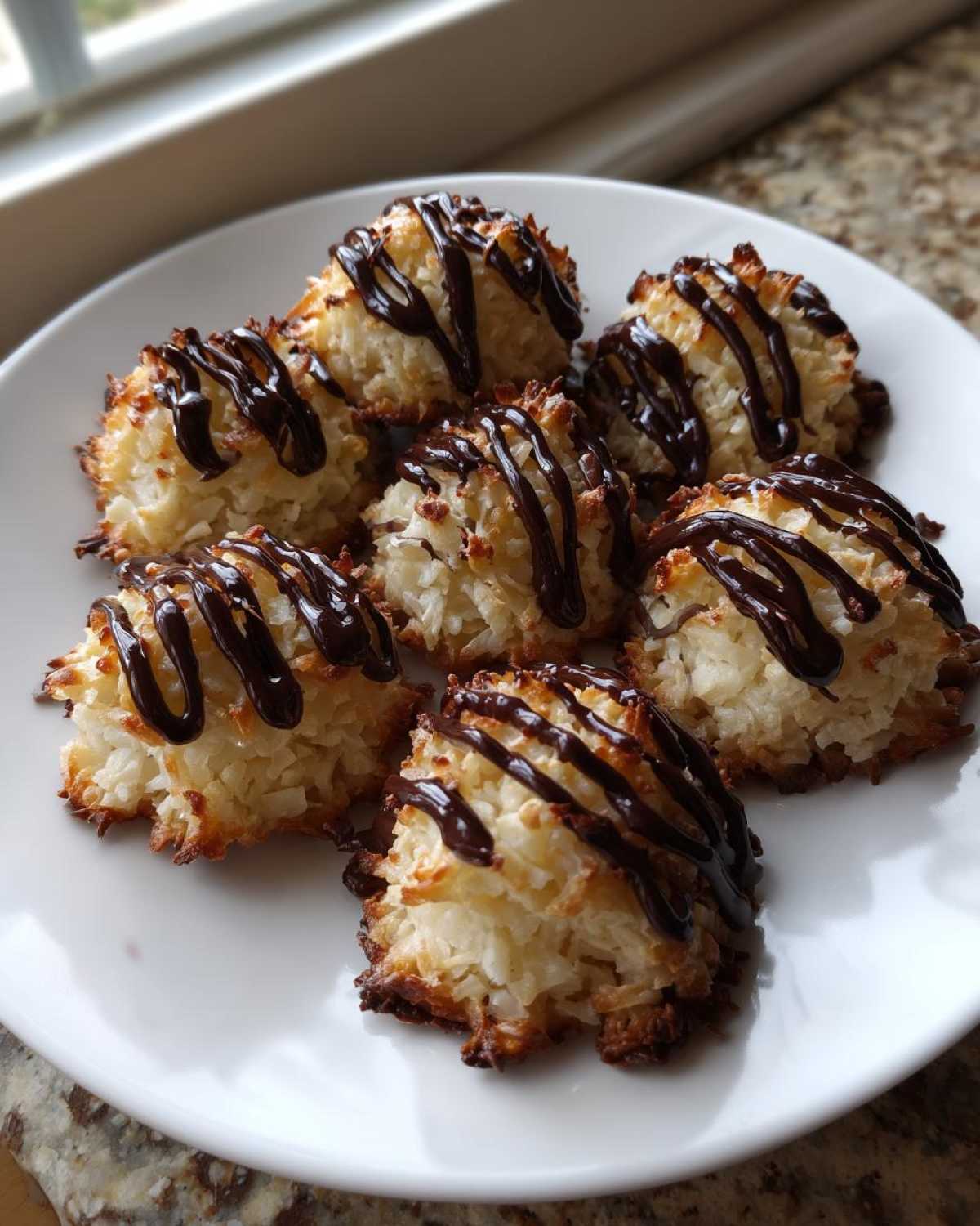 Six golden-brown Coconut Macaroons with Dark Chocolate Drizzle arranged on a white plate.