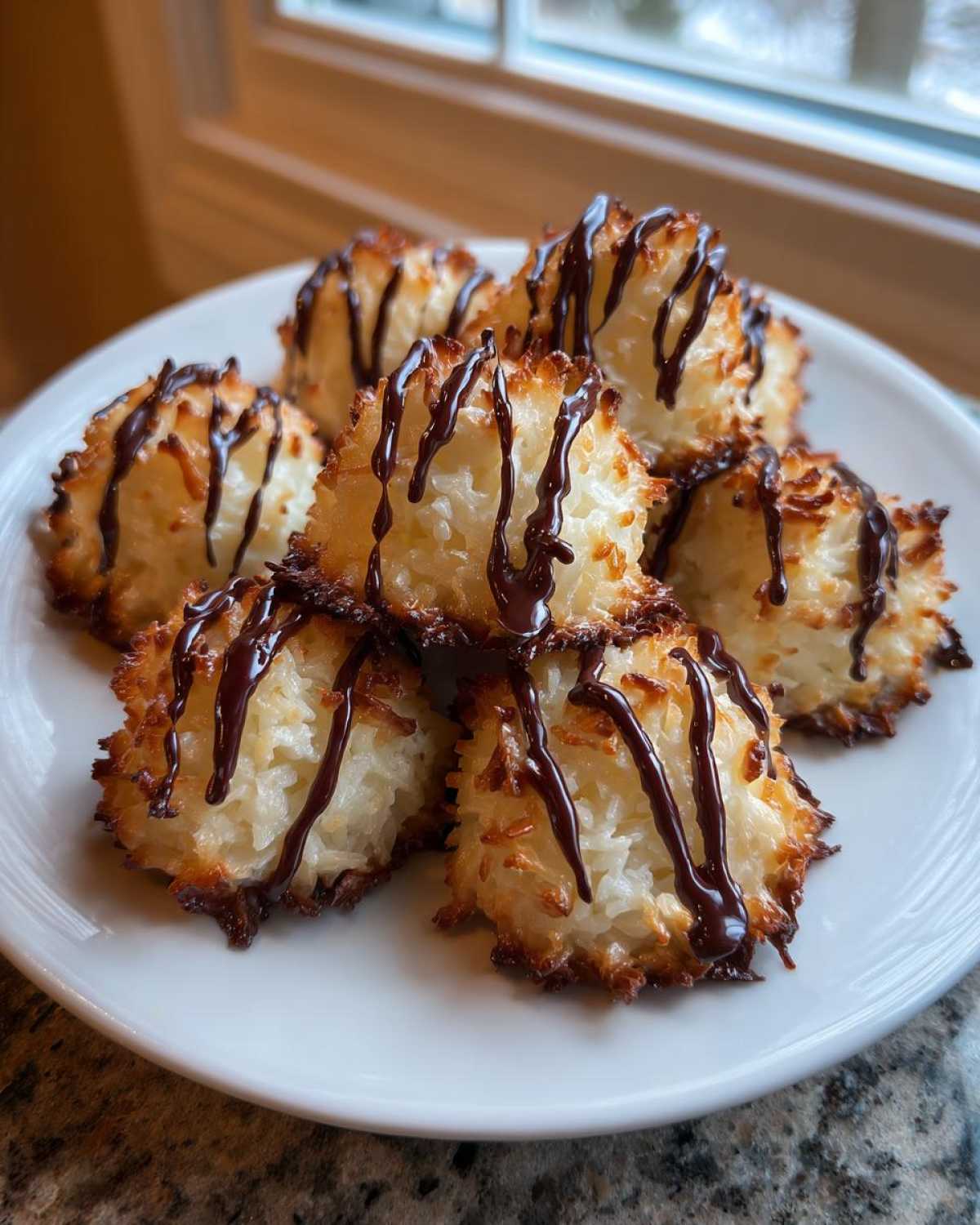 A stack of golden-brown Coconut Macaroons with Dark Chocolate Drizzle on a white plate.