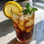 A tall glass filled with iced Cold Brew Lemonade, garnished with a lemon wheel and fresh mint sprigs.