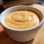 Close-up of creamy, orange-hued Copycat Raising Cane’s Sauce, topped with black pepper, in a white ramekin.