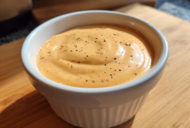 Close-up of creamy, orange-hued Copycat Raising Cane’s Sauce, topped with black pepper, in a white ramekin.