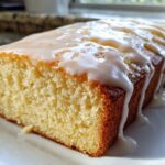 Close-up of a moist Copycat Starbucks Iced Lemon Loaf with thick white glaze dripping down the sides.