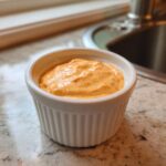 Close-up of creamy, orange Copycat Taco Bell Chicken Quesadilla Sauce in a small white ramekin.