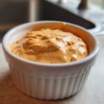 Close-up of creamy, orange-hued Copycat Taco Bell Chicken Quesadilla Sauce in a white fluted ramekin.