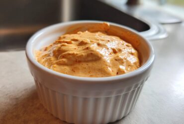 Close-up of creamy, orange-hued Copycat Taco Bell Chicken Quesadilla Sauce in a white fluted ramekin.