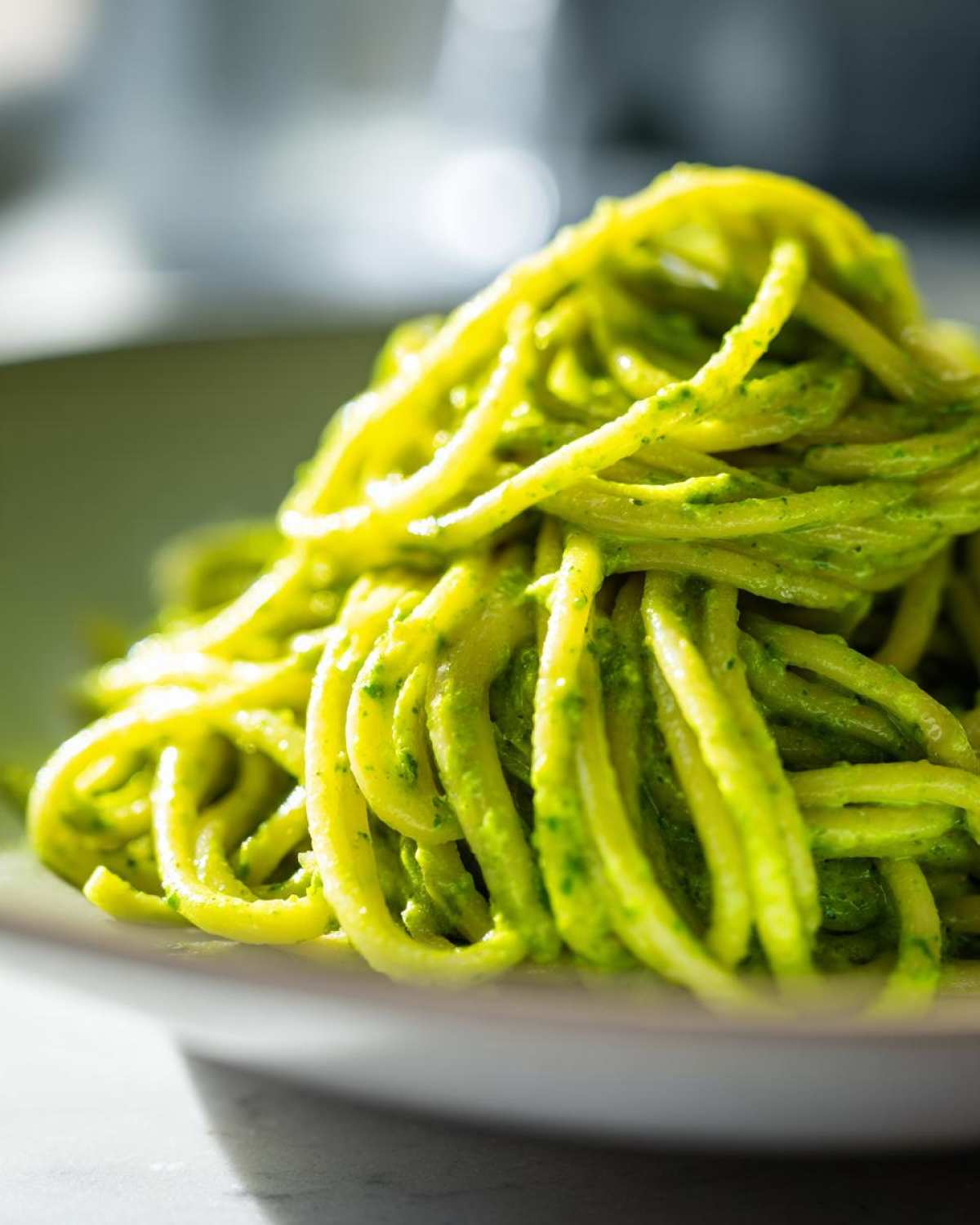 A close-up shot of bright green, sauced spaghetti noodles representing Creamy Avocado Pasta served in a light-colored bowl.