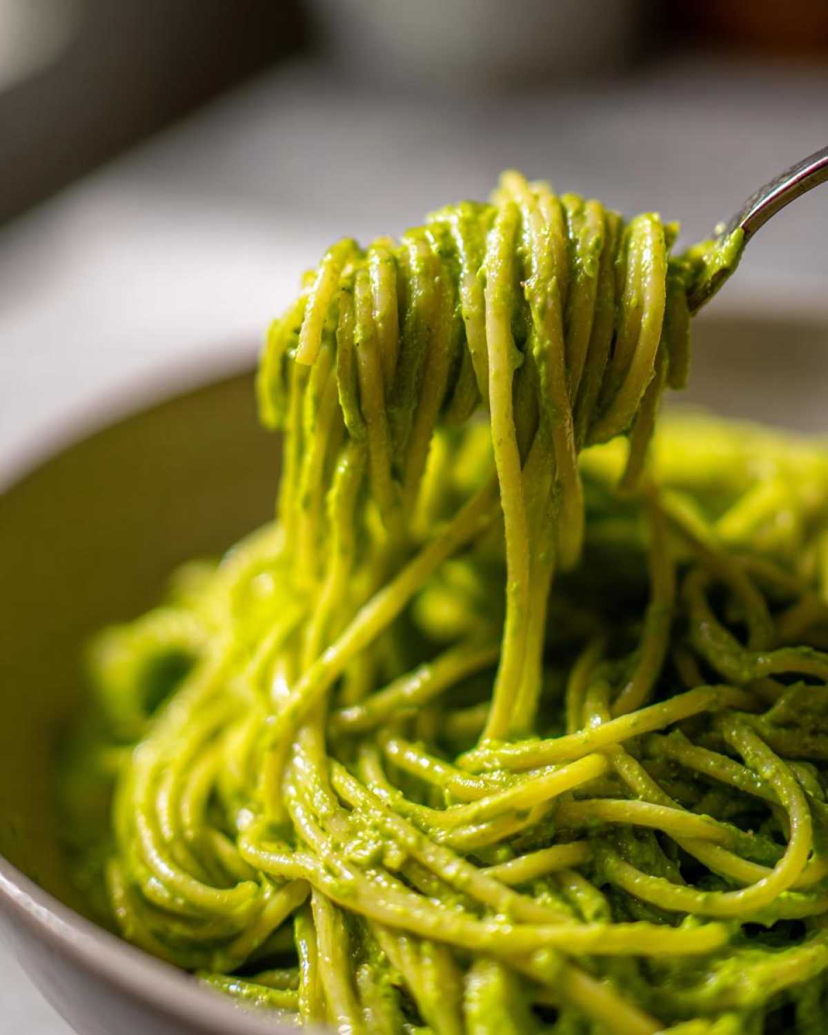 A fork lifts a generous twirl of spaghetti coated in vibrant green Creamy Avocado Pasta sauce.