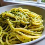 A close-up of spaghetti coated in vibrant green, creamy avocado pasta sauce served in a white bowl.