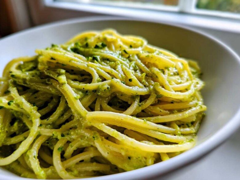 A close-up of spaghetti coated in vibrant green, creamy avocado pasta sauce served in a white bowl.