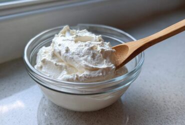 A glass bowl filled with thick, creamy white dressing, likely the base for Copycat Olive Garden Salad Dressing, with a wooden spoon resting in it.
