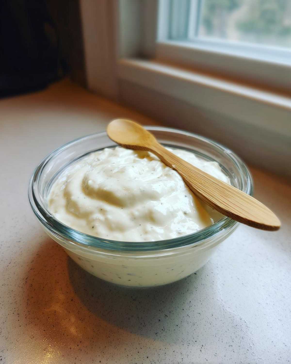 A glass bowl filled with thick, creamy Copycat Olive Garden Salad Dressing, topped with a small wooden spoon.