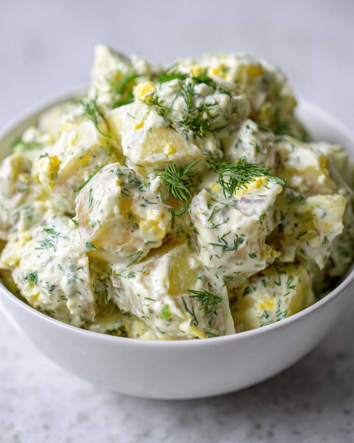 Close-up of a white bowl filled with Creamy Dill Potato Salad, featuring chunks of potato, creamy dressing, and fresh dill.