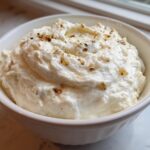 A white bowl filled with fluffy Creamy Garlic Mashed Cauliflower, topped with herbs and browned garlic bits.