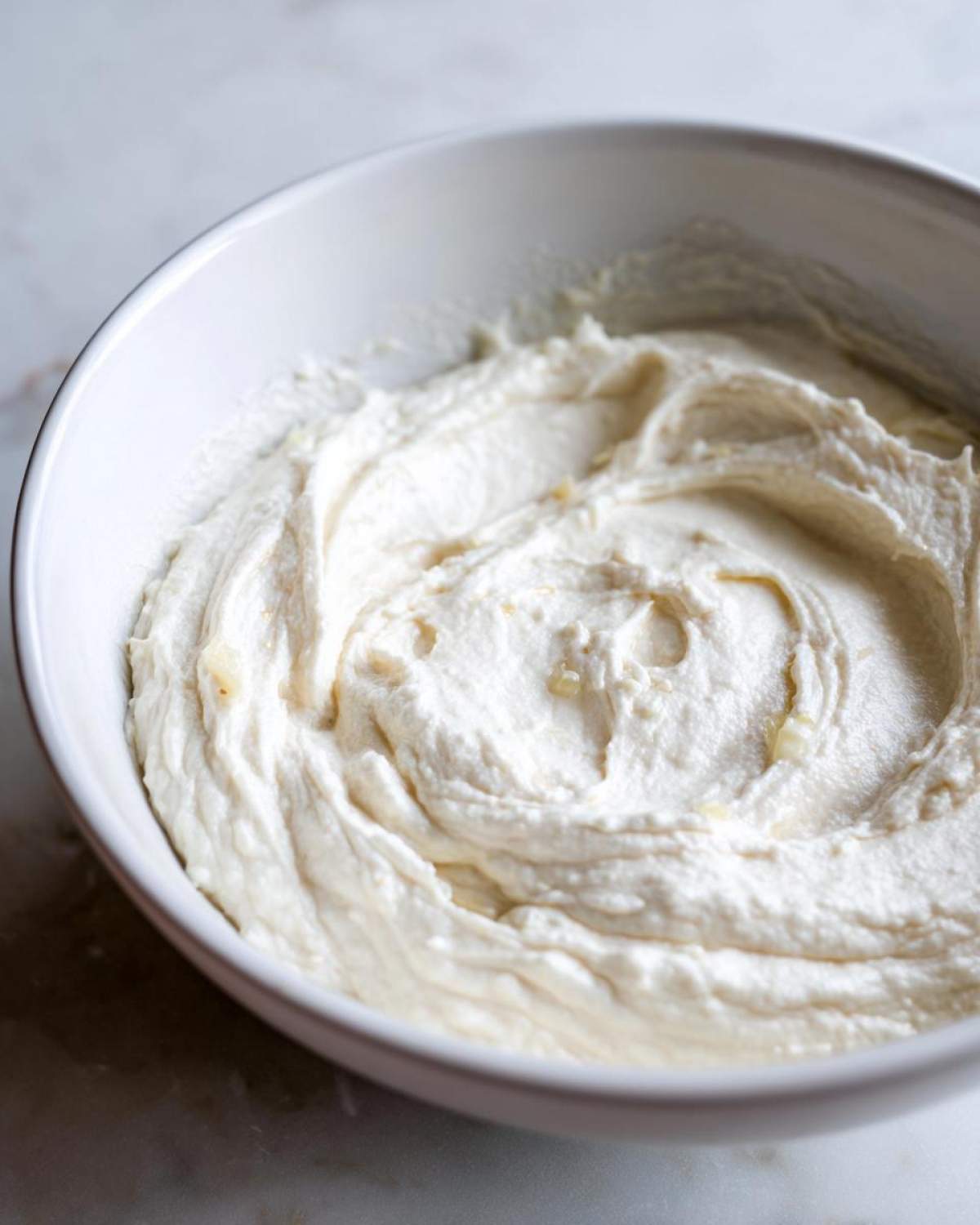 A close-up of smooth, white Creamy Garlic Mashed Cauliflower swirled in a white bowl.