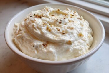 A white bowl filled with fluffy Creamy Garlic Mashed Cauliflower, topped with herbs and browned garlic bits.