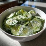 Close-up of sliced cucumbers coated in a white, creamy dressing and topped with fresh dill, representing Creamy German Cucumber Salad.
