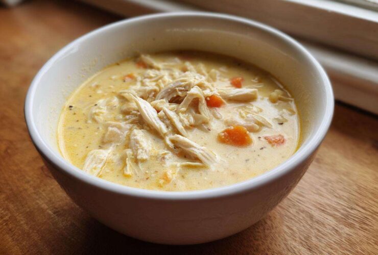 Close-up of a white bowl filled with Creamy Lemon Chicken Orzo Soup, featuring shredded chicken and visible carrot pieces.