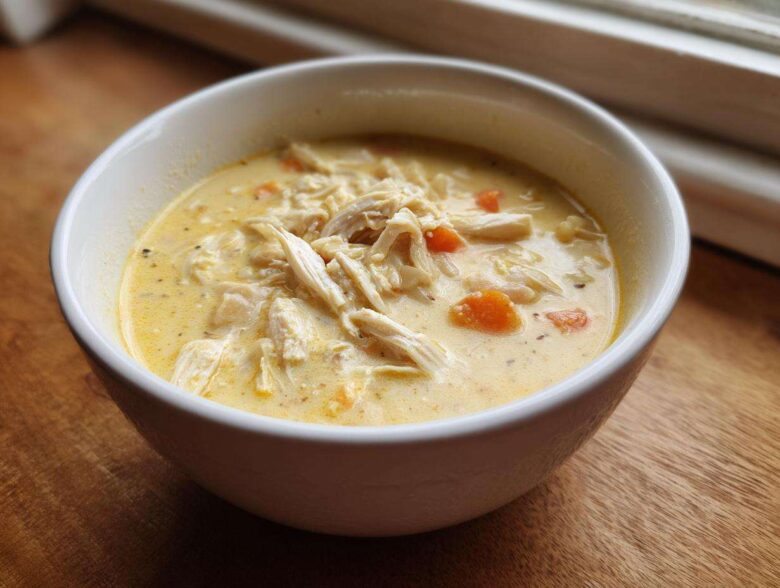 Close-up of a white bowl filled with Creamy Lemon Chicken Orzo Soup, featuring shredded chicken and visible carrot pieces.