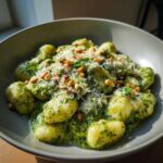 Close-up of tender gnocchi coated in creamy pesto sauce, topped with grated cheese and pine nuts.
