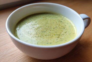 Close-up of a white mug filled with light green, creamy potato leek soup, garnished with herbs.
