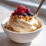 A close-up of a thick Creamy Vanilla Protein Smoothie Bowl topped with frozen raspberries, blueberries, and granola.