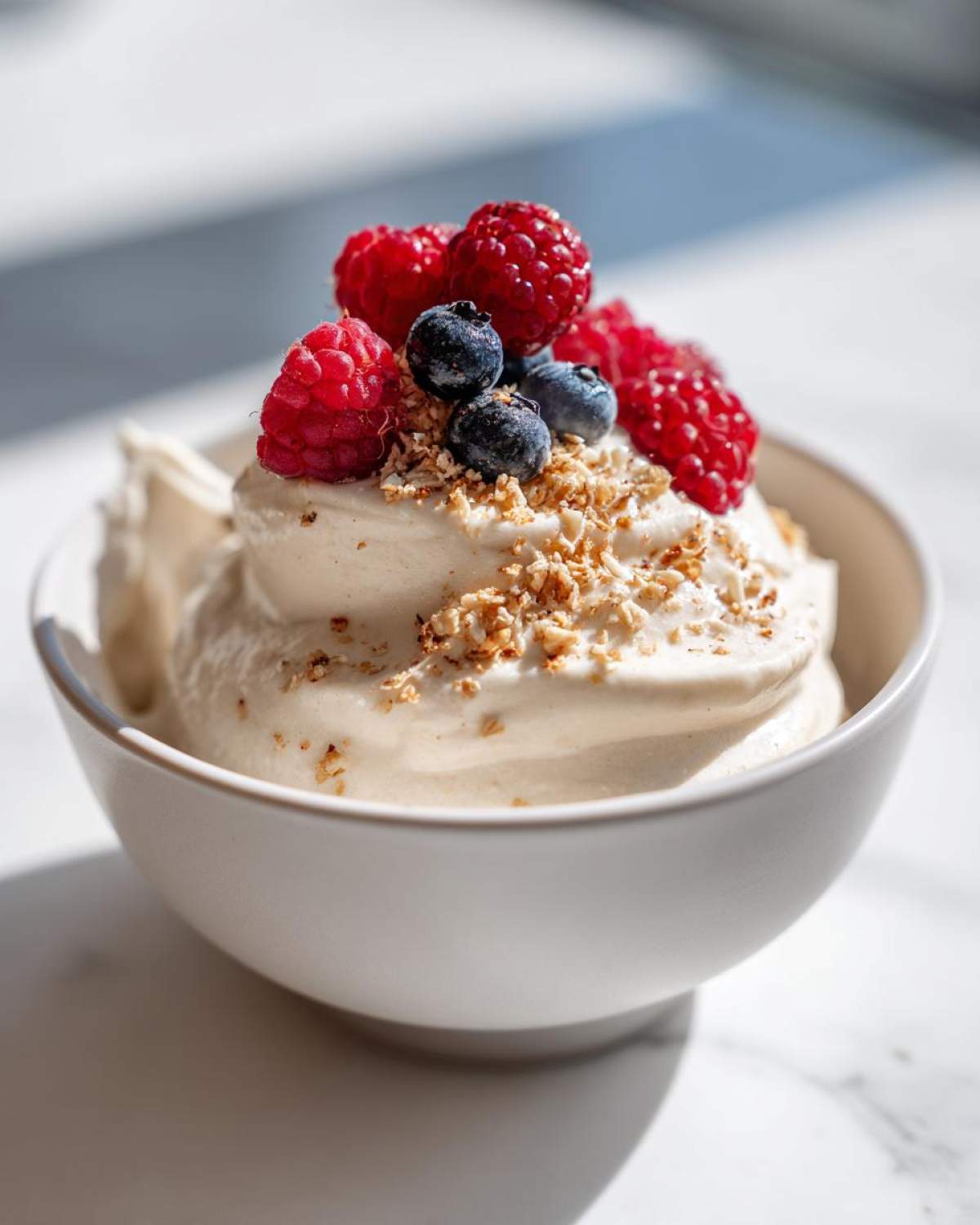 A serving of Creamy Vanilla Protein Smoothie Bowl topped with fresh raspberries, blueberries, and crushed nuts.