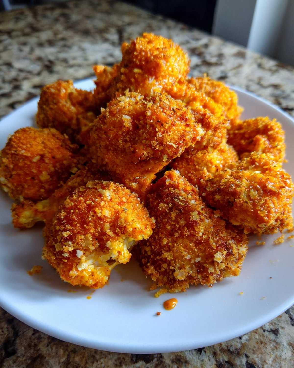 A pile of golden-orange, breaded Crispy Air Fryer Cauliflower Wings served on a white plate.