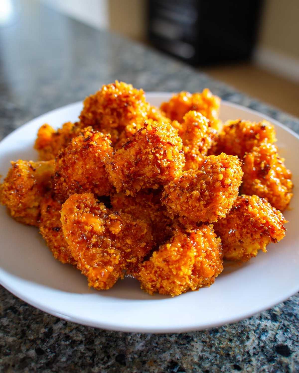 A white plate piled high with golden-brown, crispy air fryer cauliflower wings coated in a shiny sauce.