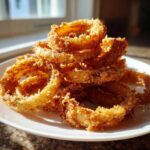 A stack of golden brown, crispy Air Fryer Onion Rings piled high on a white plate.