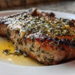 Close-up of a juicy, crispy air fryer pork chop topped with melted garlic butter and herbs.