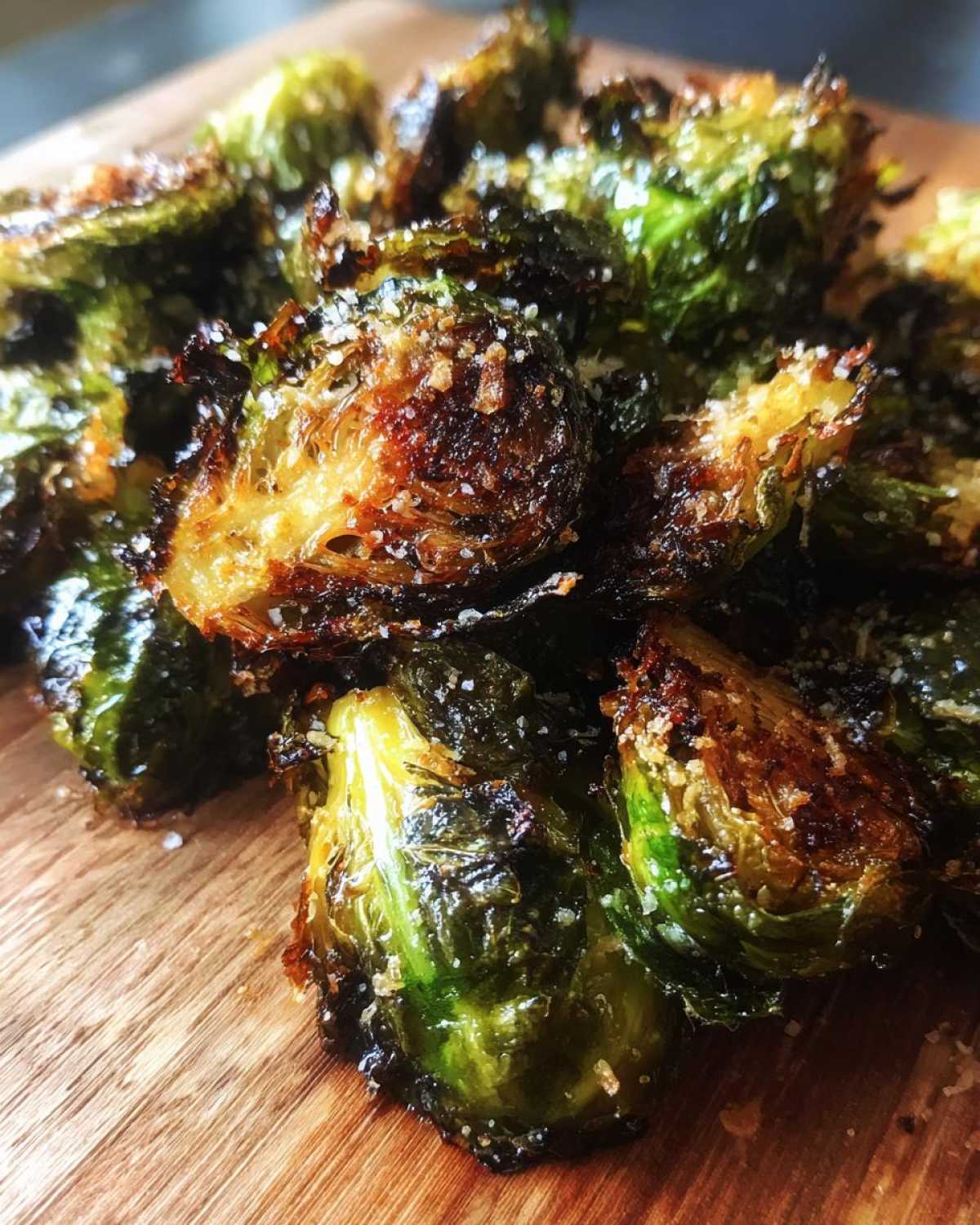 Close-up of deeply roasted Crispy Parmesan Brussels Sprouts sprinkled with grated cheese on a wooden board.