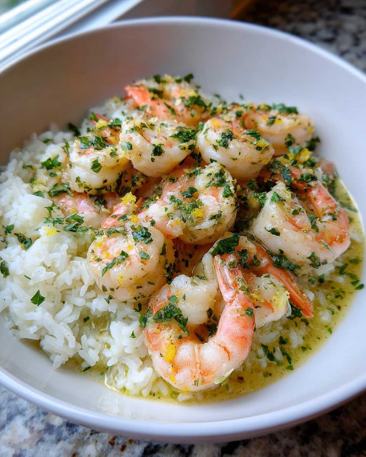 Plump shrimp coated in garlic butter sauce and parsley served over white rice in a white bowl, perfect for Garlic Butter Shrimp and Rice Skillet.