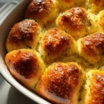 Close-up of golden brown Garlic Parmesan Pull-Apart Bread rolls soaking in melted butter and herbs in a white baking dish.