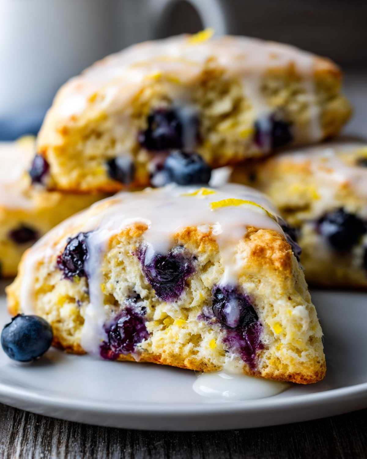 Close-up of a moist Blueberry Lemon Scones wedge topped with white glaze and lemon zest, served with fresh blueberries.