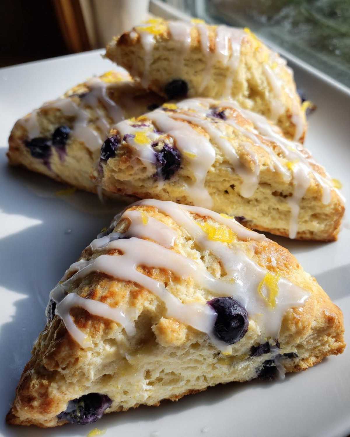 Close-up of several freshly baked Blueberry Lemon Scones drizzled with white glaze and lemon zest.