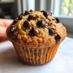 A close-up, appetizing shot of a freshly baked Gluten-Free Banana Chocolate Chip Muffin topped generously with melted chocolate chips.