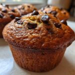 A close-up of a freshly baked Gluten-Free Banana Chocolate Chip Muffin topped with melted chocolate chips.