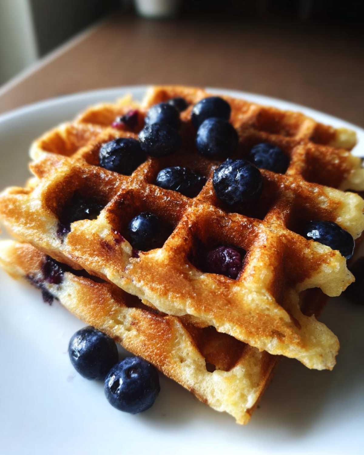 Close-up of two stacked Gluten-Free Blueberry Waffles topped with fresh blueberries on a white plate.