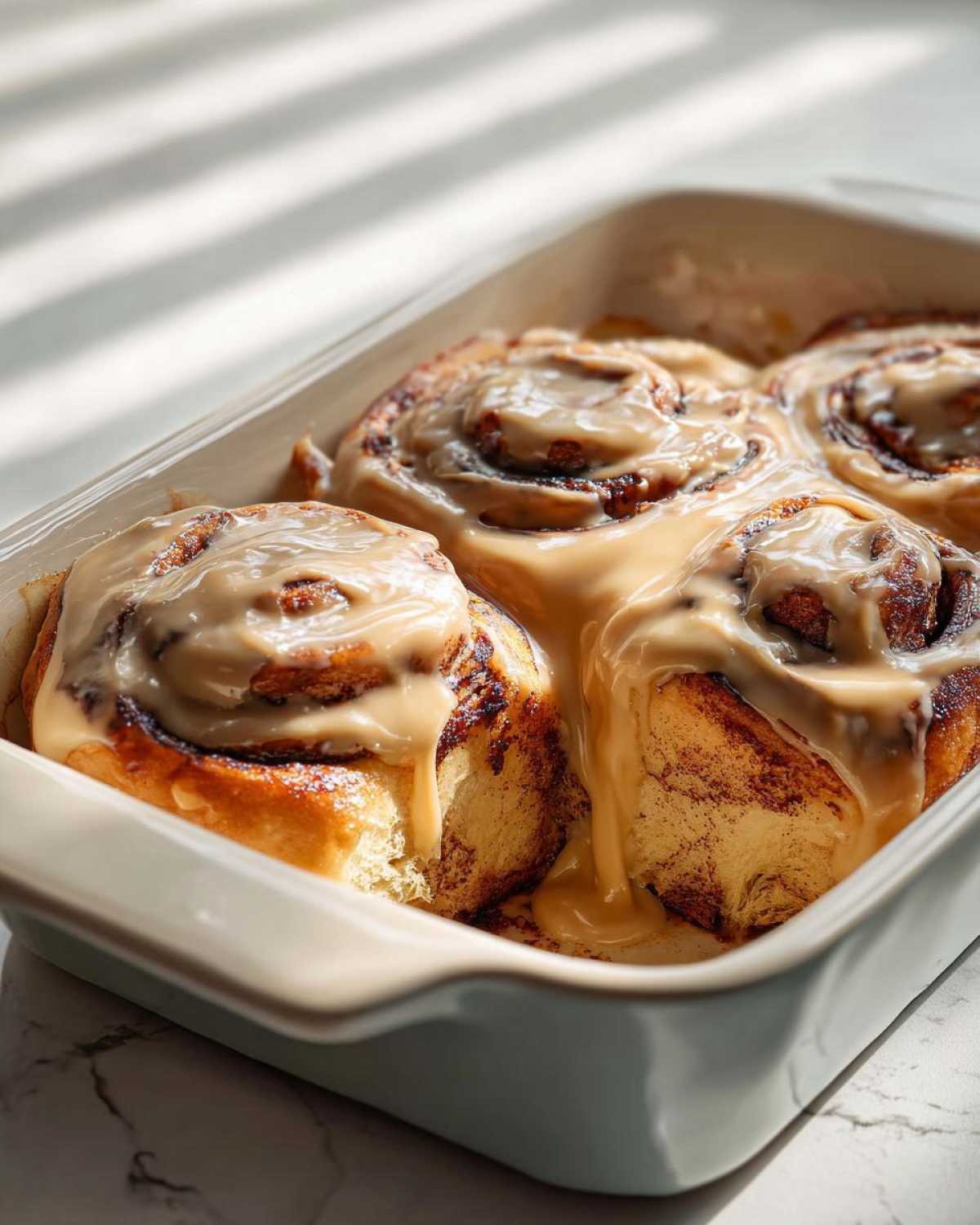 Close-up of warm Gluten-Free Cinnamon Rolls generously topped with dripping caramel-colored icing in a light blue baking dish.