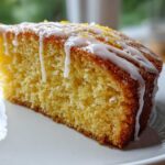 Close-up of a moist slice of Gluten-Free Lemon Coconut Cake topped with white lemon glaze and zest.
